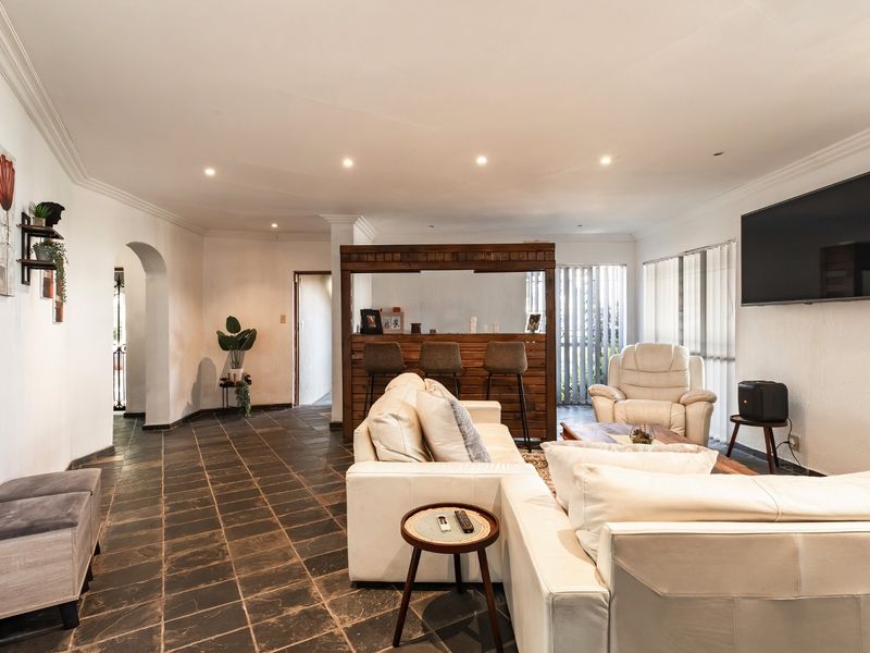 Spacious living room featuring dark tiled flooring, recessed downlighting, an arched entryway, and a built-in wooden bar area.