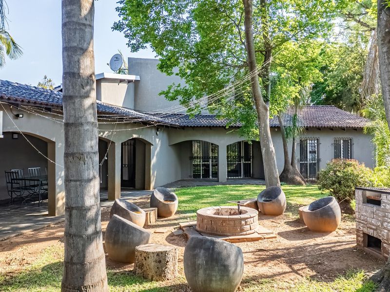 Spacious rear garden featuring a covered patio, built-in braai, and a central brick fire pit area, ideal for outdoor entertaining.