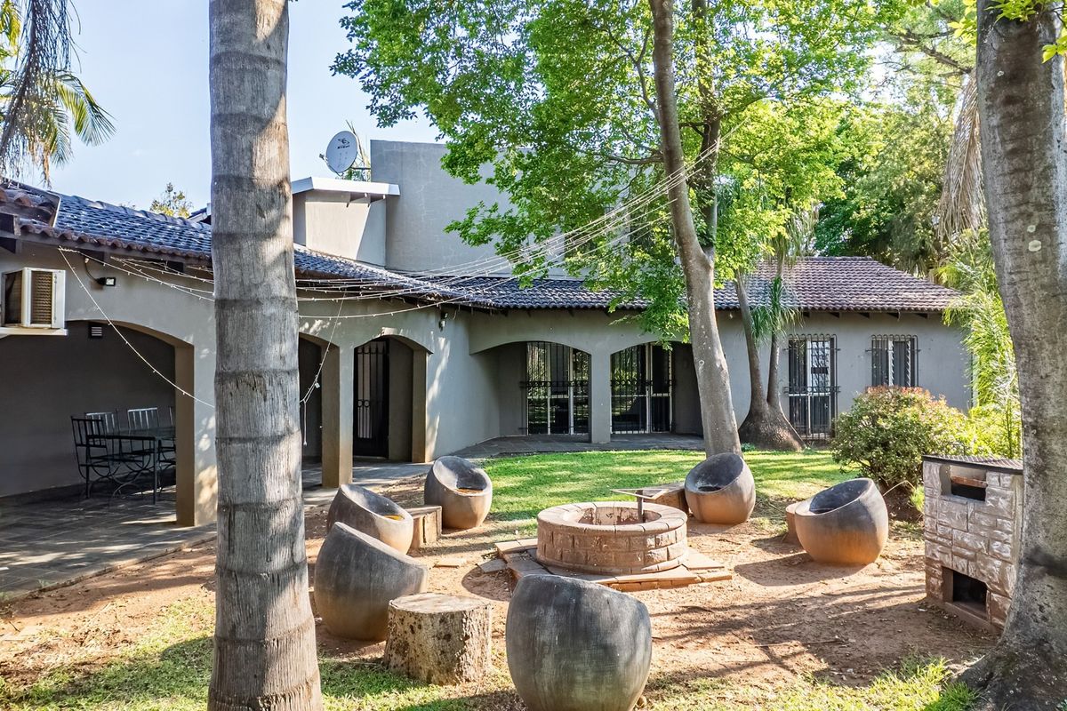 Spacious rear garden featuring a covered patio, built-in braai, and a central brick fire pit area, ideal for outdoor entertaining.