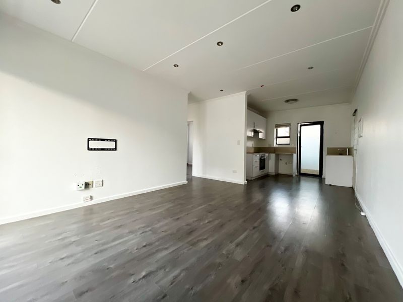 Spacious open-plan living area featuring modern laminate flooring, recessed lighting, and a functional kitchen with built-in cabinetry and appliances.