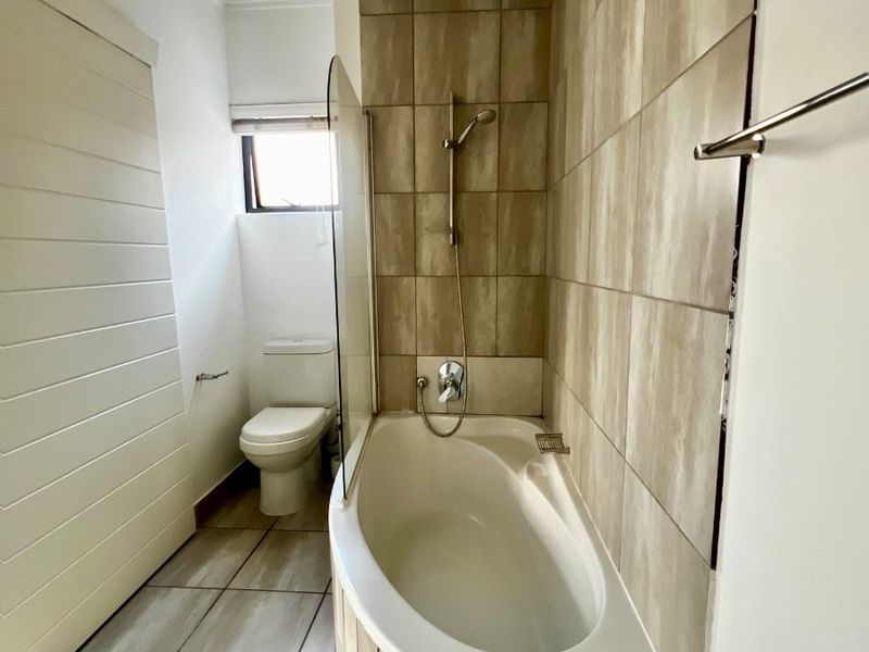 A clean, functional bathroom featuring a built-in bathtub with a glass shower screen, tiled wall finishes, and a standard toilet.
