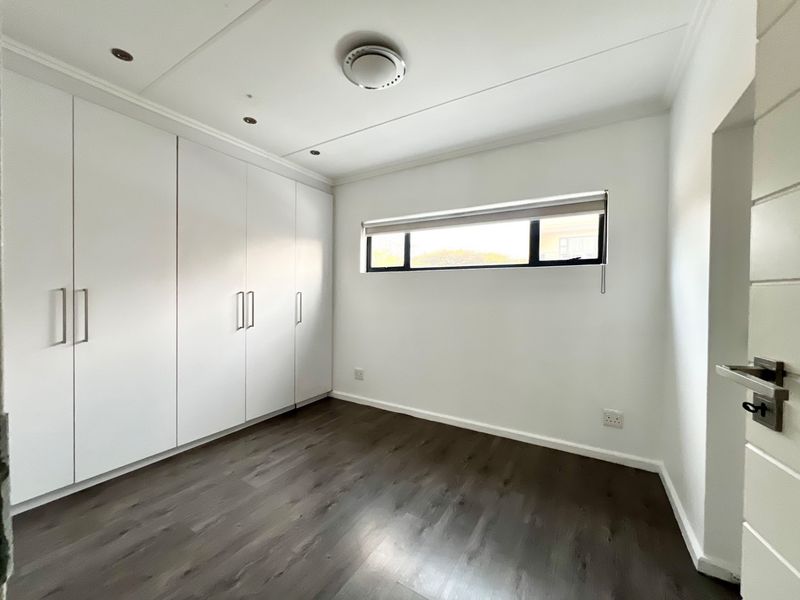 A bright, empty bedroom featuring modern laminate flooring, ample built-in cupboard storage, and recessed ceiling lighting.