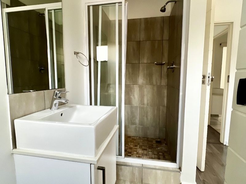 A clean and modern bathroom featuring a vanity with a basin, a glass-enclosed shower with tiled walls, and neutral floor tiling.