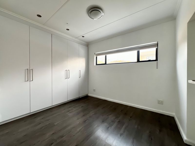 A clean, empty bedroom featuring dark laminate flooring, ample built-in cupboard storage, and a horizontal window providing natural light.