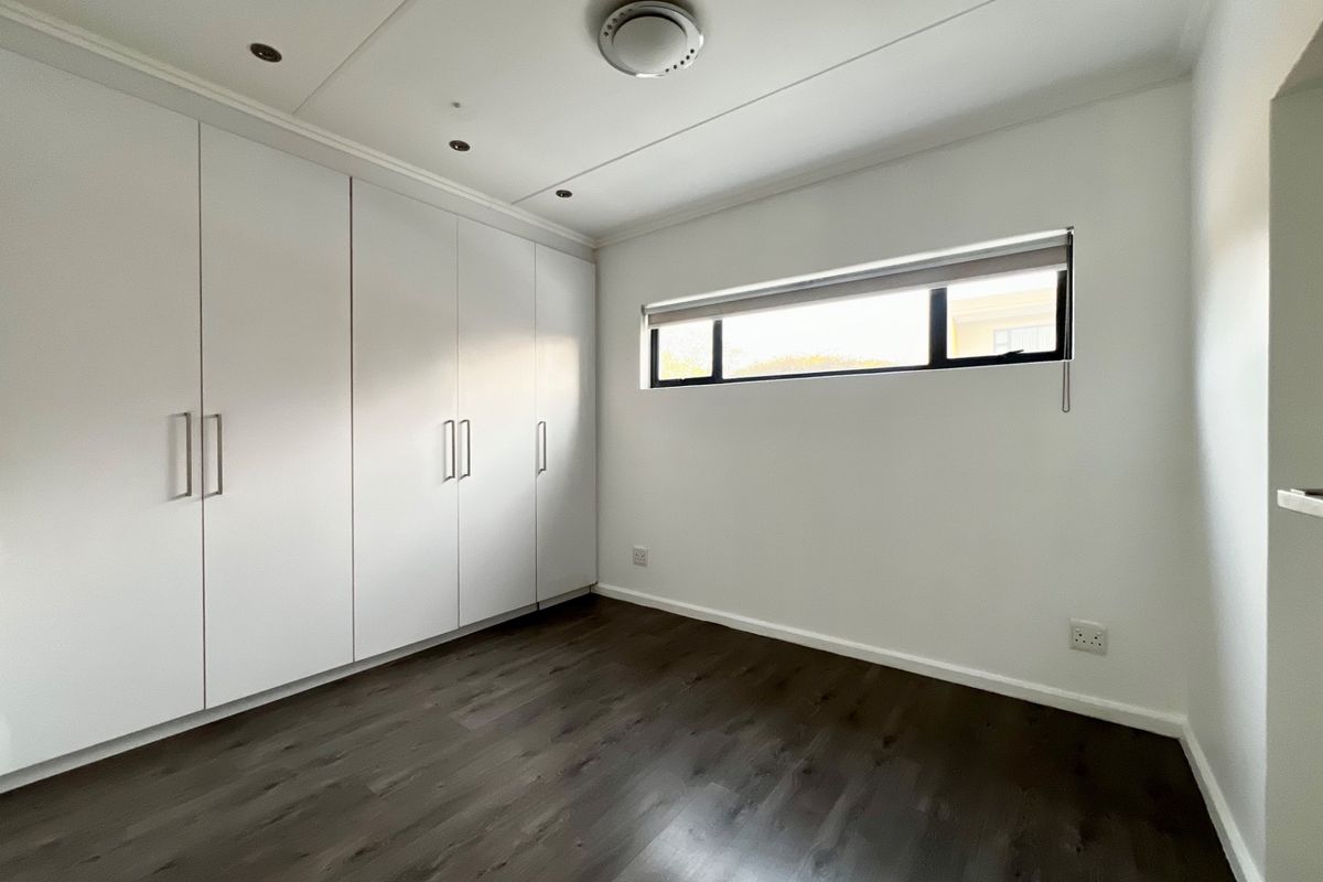 A clean, empty bedroom featuring dark laminate flooring, ample built-in cupboard storage, and a horizontal window providing natural light.