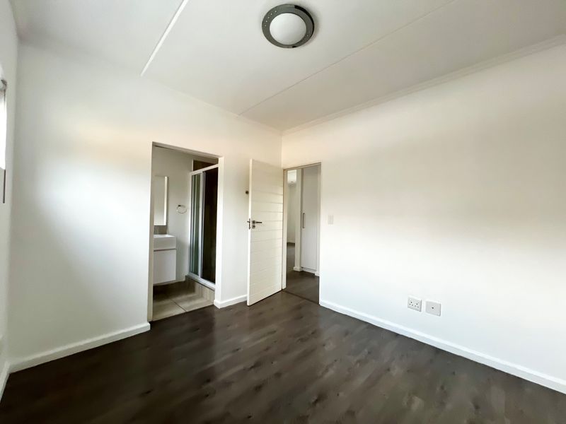 A clean, empty bedroom featuring dark laminate flooring, neutral white walls, and direct access to an en-suite bathroom.