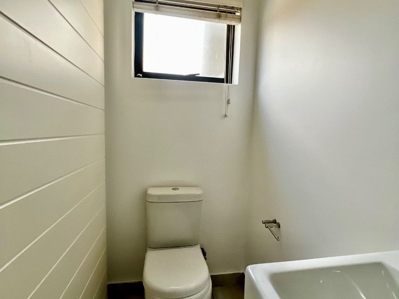 A clean and functional guest bathroom featuring a toilet, washbasin, tiled flooring, and a window with a fitted blind.