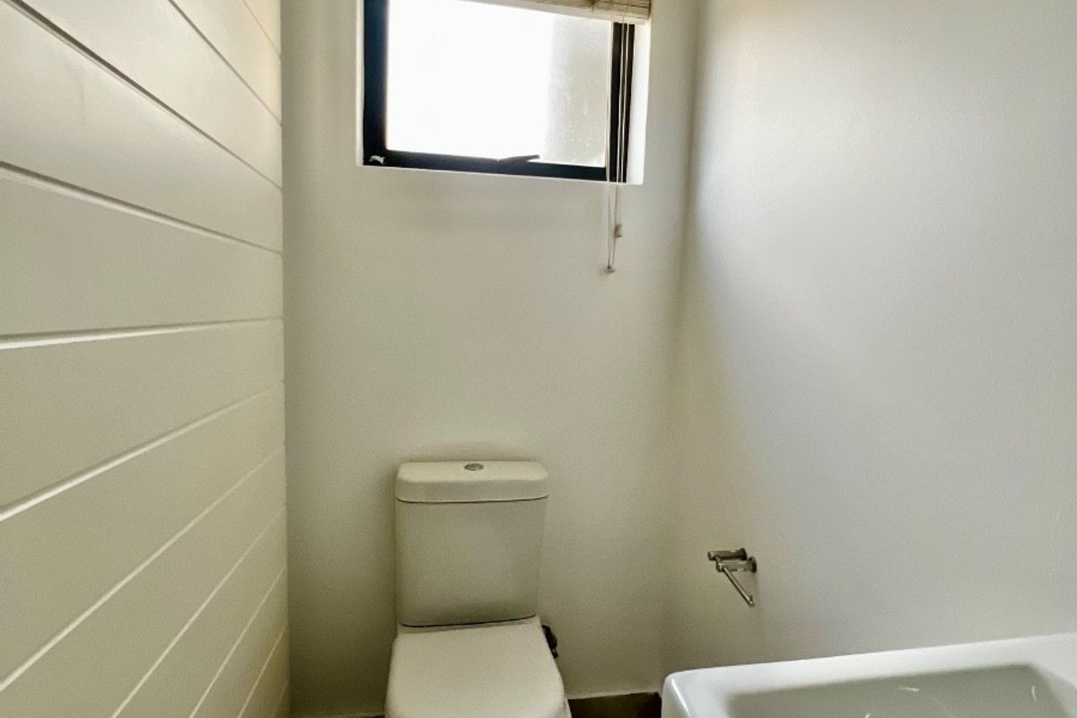 A clean and functional guest bathroom featuring a toilet, washbasin, tiled flooring, and a window with a fitted blind.