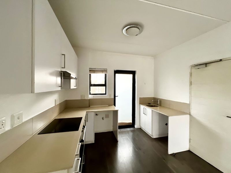 A clean, modern kitchen featuring white cabinetry, laminate countertops, an integrated electric hob, and dark laminate flooring with direct access to an outdoor area.