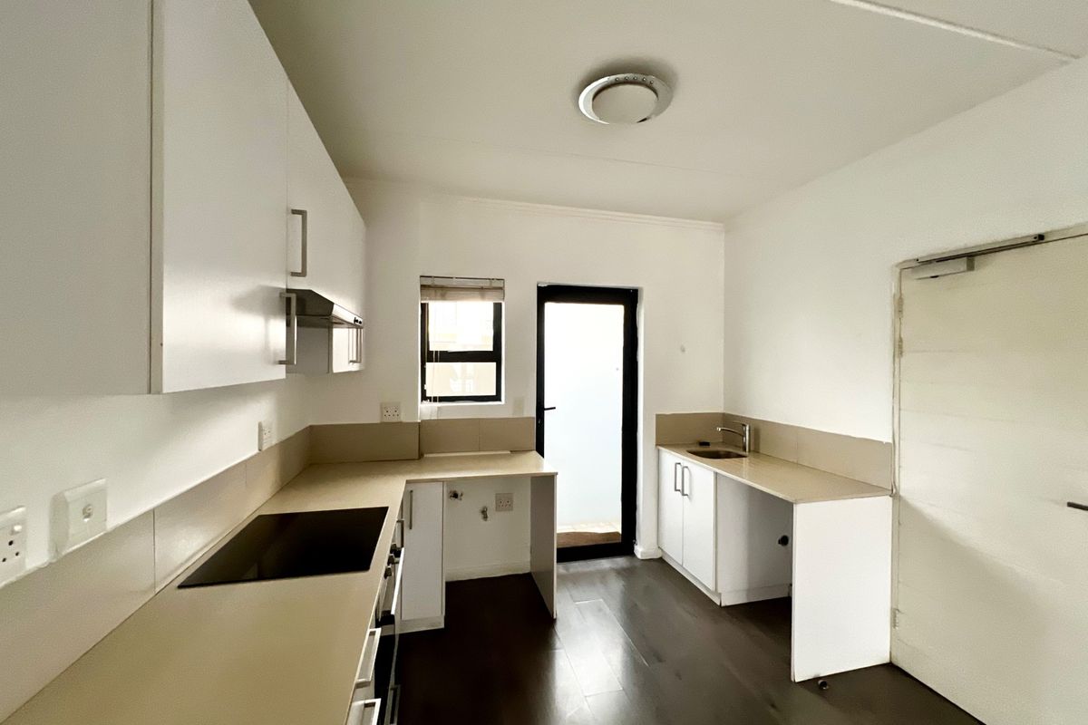 A clean, modern kitchen featuring white cabinetry, laminate countertops, an integrated electric hob, and dark laminate flooring with direct access to an outdoor area.