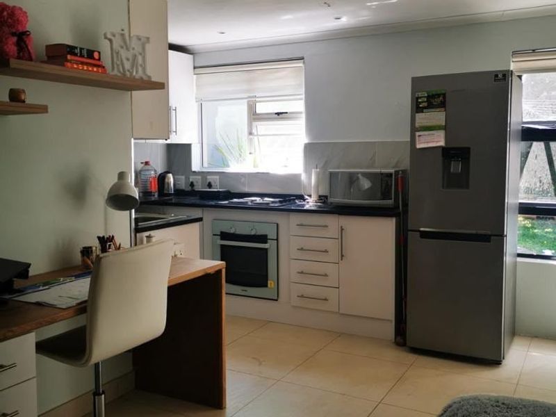 Open-plan kitchen and workspace area featuring modern cabinetry, stone countertops, built-in oven, and tiled flooring in a well-lit, functional layout.
