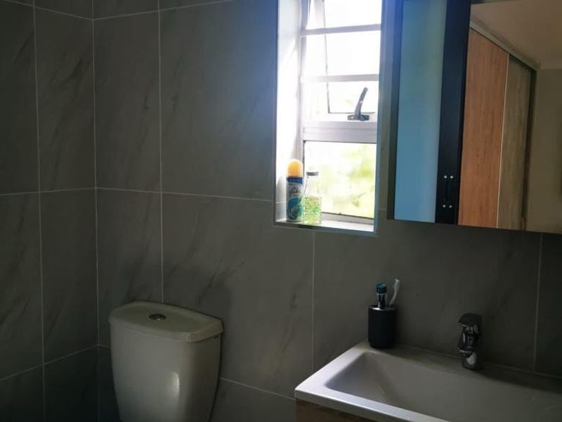 A modern bathroom featuring grey wall tiles, a vanity with a basin, and a louver window providing natural light.