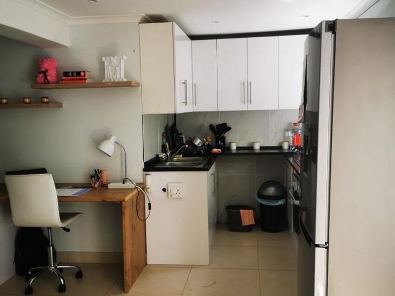 Compact kitchen featuring white cabinetry, dark countertops, tiled flooring, and an integrated workspace area with floating shelving.