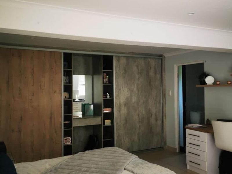 A well-maintained bedroom featuring modern built-in sliding wardrobes with integrated shelving, recessed ceiling lighting, and neutral tiled flooring.