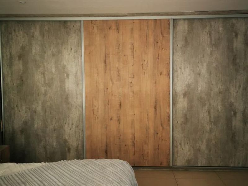 A bedroom featuring modern built-in sliding door wardrobes with a mix of wood-grain and concrete-effect finishes, complemented by tiled flooring.