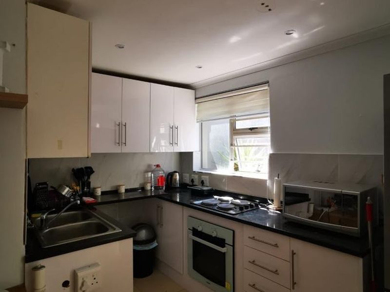 A functional kitchen featuring white cabinetry, dark countertops, integrated oven, hob, and a stainless steel sink with tiled backsplash.