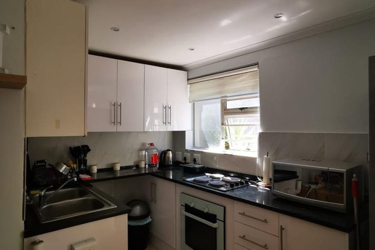 A functional kitchen featuring white cabinetry, dark countertops, integrated oven, hob, and a stainless steel sink with tiled backsplash.