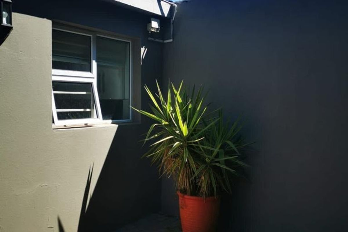 A private rear courtyard area featuring paved flooring, modern grey exterior walls, and a window looking into the property.