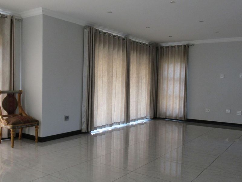 Spacious, light-filled living area featuring polished tiled flooring, recessed downlighting, and large glass doors providing ample natural light.