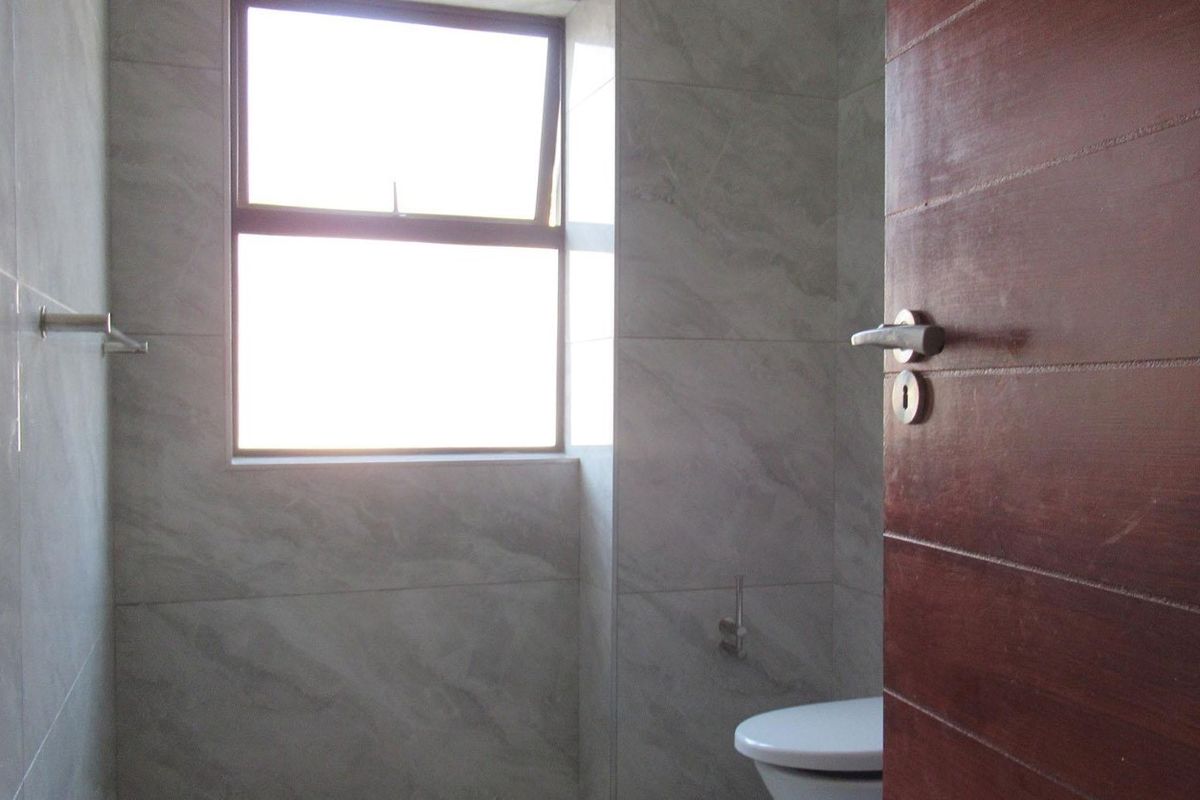 A clean, modern bathroom featuring neutral marble-look wall tiles, a top-hung window for natural light, and a solid wood door.