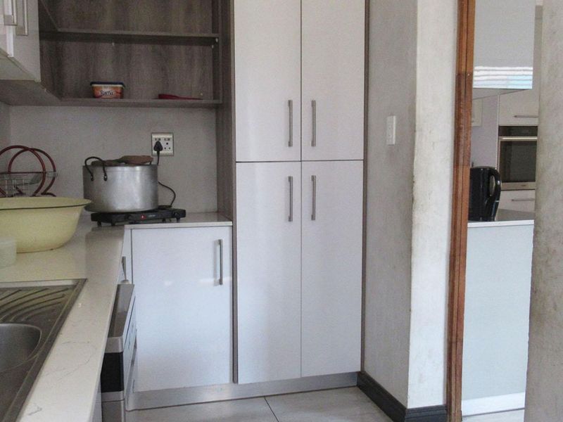 A functional kitchen area featuring white built-in cabinetry, stone countertops, and a stainless steel sink, with a view into an adjacent kitchen space.