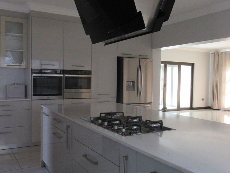 Modern open-plan kitchen featuring a central island with a gas hob, stone countertops, integrated appliances, and sleek cabinetry, flowing into the adjacent living area.