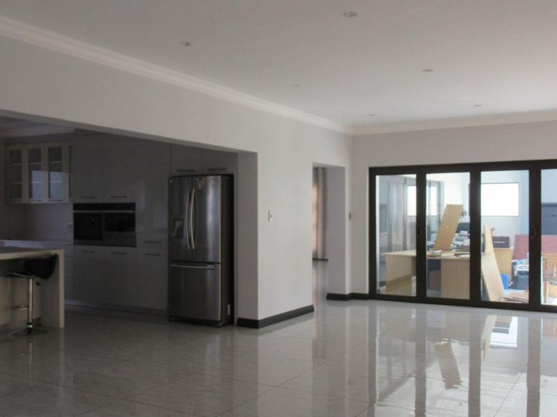 Spacious open-plan living area featuring polished tile flooring, recessed lighting, and a modern kitchen with built-in appliances, leading to an adjacent room via bi-fold doors.