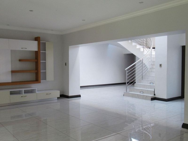 Spacious open-plan living area featuring polished tiled floors, built-in cabinetry, and a modern spiral staircase with a metal balustrade.