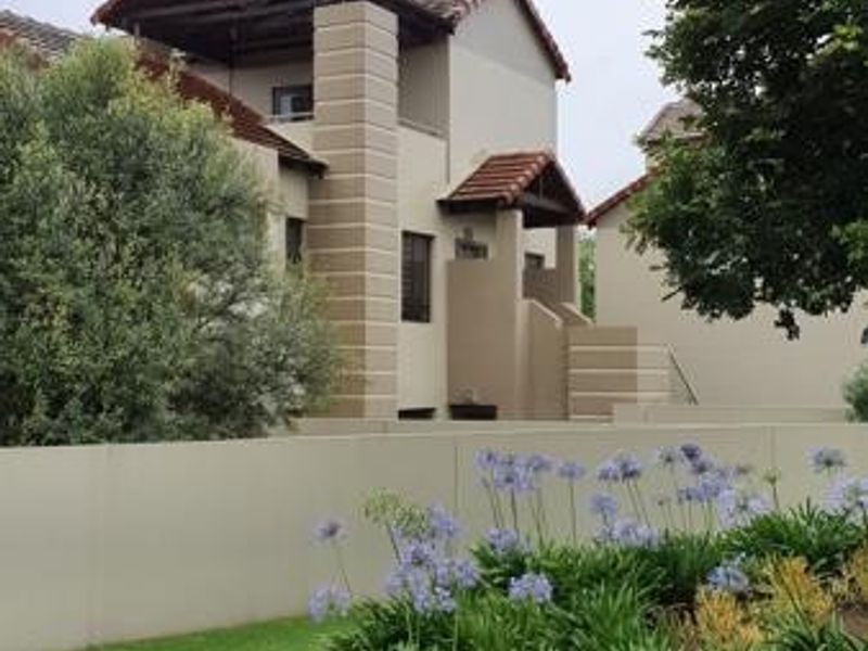 A view of the townhouse exterior featuring a well-maintained garden, boundary wall, and tiled roof architecture.