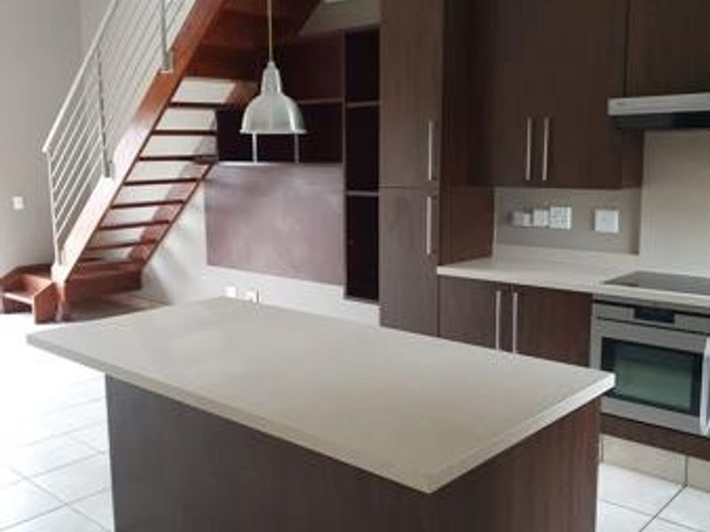 Modern open-plan kitchen featuring dark wood cabinetry, a central island, and a striking wooden staircase leading to the upper level.