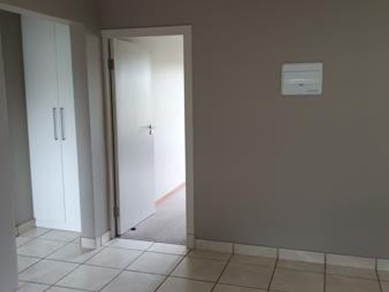 A clean, empty hallway featuring neutral tiled flooring, built-in storage cupboards, and access to an adjoining room.