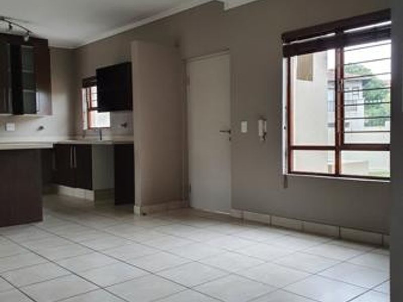 Open plan living area featuring tiled flooring, built-in kitchen cabinetry, and a window with security bars, offering a functional and versatile space.