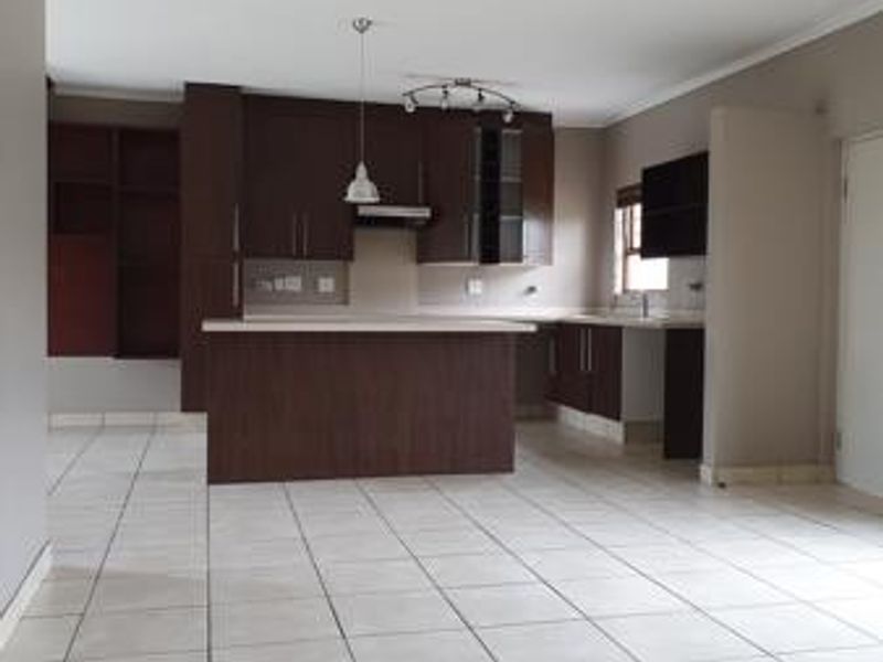 Spacious open-plan kitchen featuring dark wood cabinetry, a central island, and neutral tiled flooring throughout the living area.
