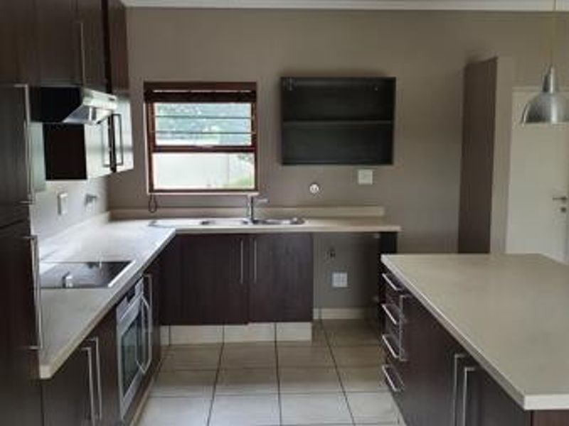 Modern kitchen featuring dark wood cabinetry, stone countertops, integrated oven, electric cooktop, and tiled flooring in a clean, functional layout.