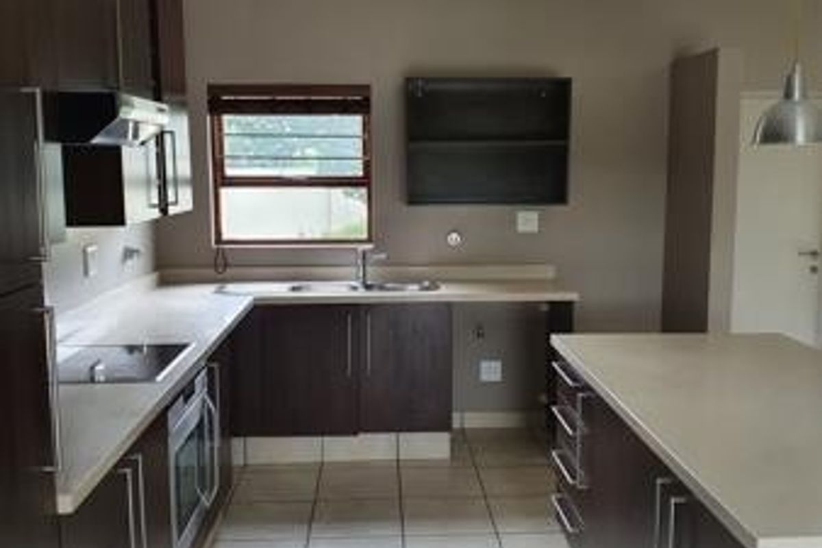Modern kitchen featuring dark wood cabinetry, stone countertops, integrated oven, electric cooktop, and tiled flooring in a clean, functional layout.