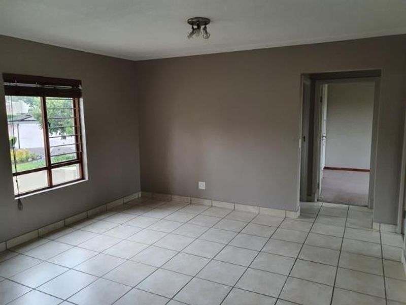 An empty living room featuring neutral wall paint, tiled flooring, and a window with security bars, providing a clean canvas for interior design.