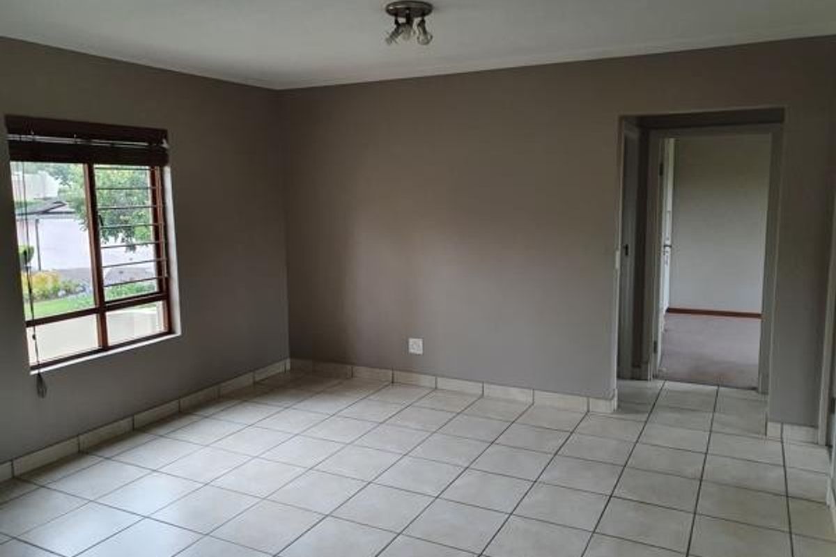 An empty living room featuring neutral wall paint, tiled flooring, and a window with security bars, providing a clean canvas for interior design.