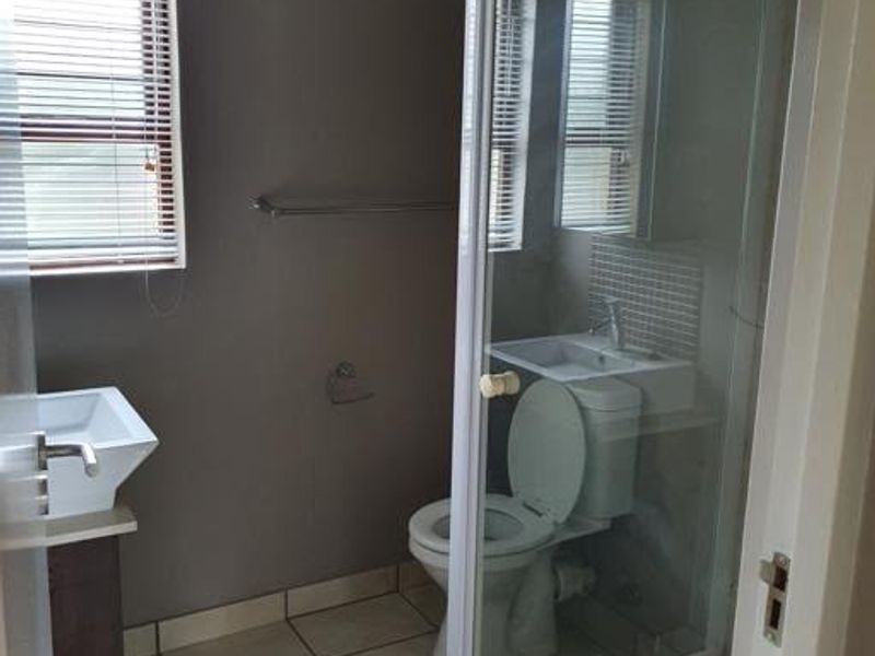 A functional bathroom featuring a glass-enclosed shower, a wall-mounted basin, and a toilet, finished with neutral wall tones and tiled flooring.
