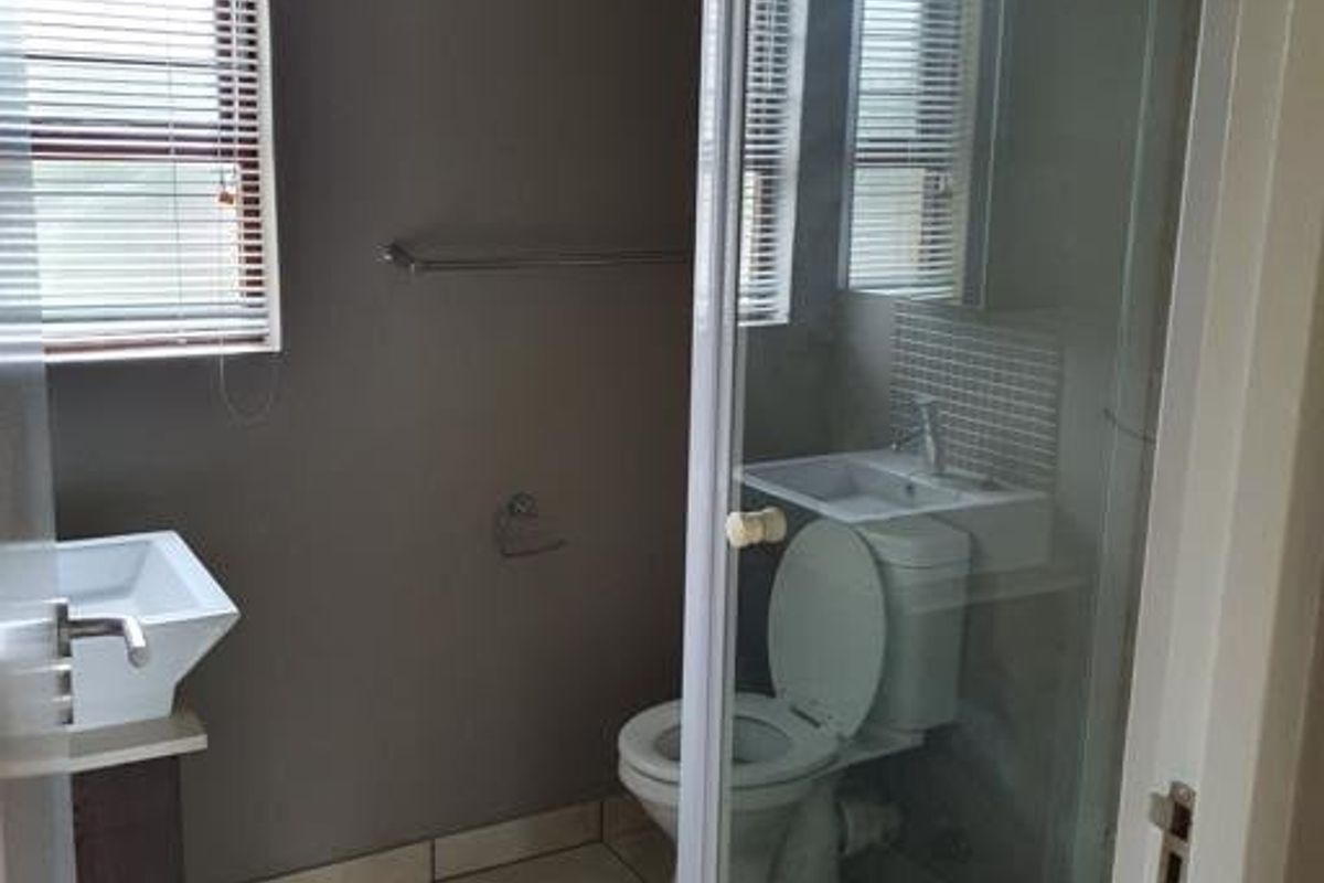 A functional bathroom featuring a glass-enclosed shower, a wall-mounted basin, and a toilet, finished with neutral wall tones and tiled flooring.