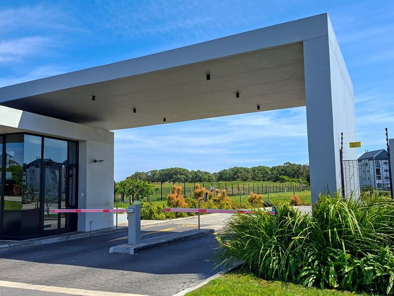 Modern security entrance gate with a guard house, paved driveway, and integrated electric fencing for the apartment complex.