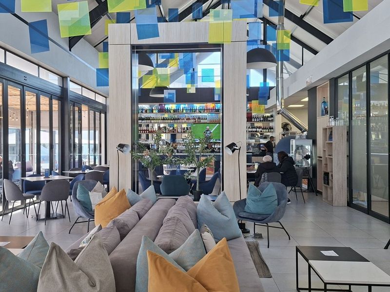 A modern, spacious clubhouse featuring vaulted ceilings with exposed rafters, a central built-in bar, and large glass sliding doors opening to an outdoor area.