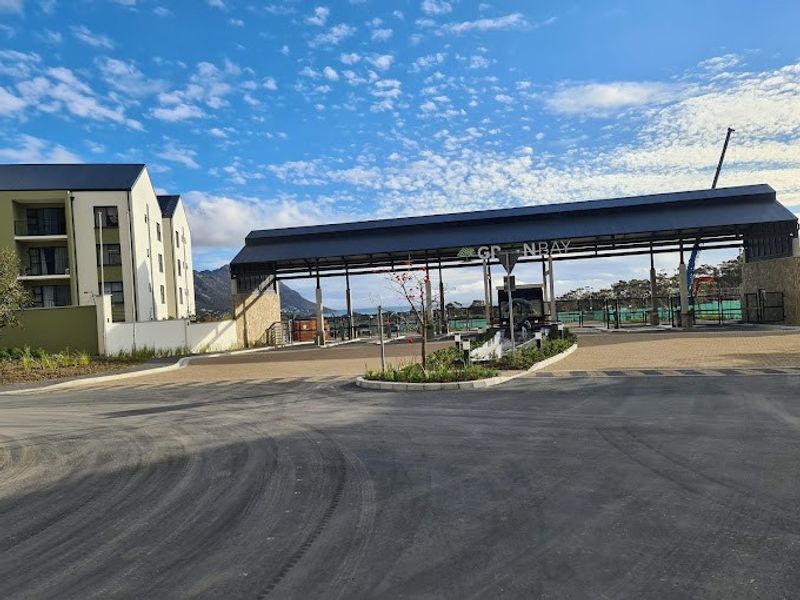 The entrance to Greenbay apartment complex featuring a modern security gatehouse, paved driveway, and well-maintained landscaping.