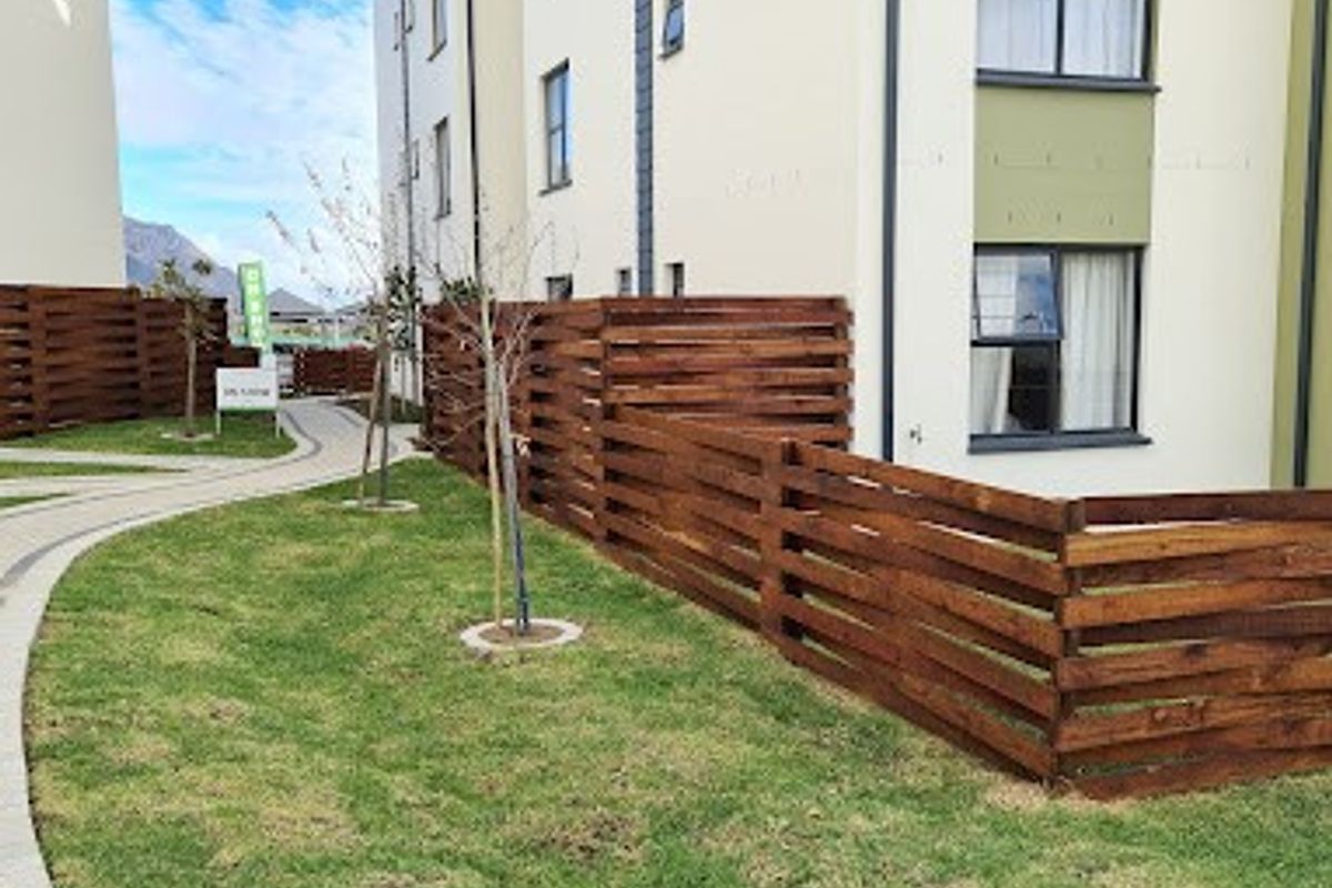 Exterior view of an apartment building featuring a well-maintained lawn, paved walkway, and modern timber slat fencing.