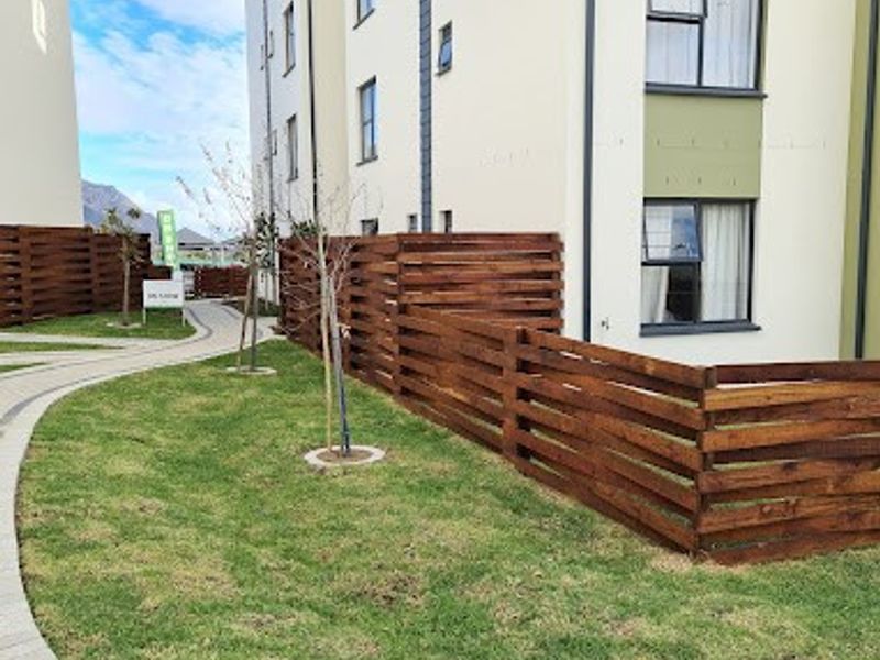 Exterior view of an apartment building featuring a well-maintained lawn, paved walkway, and modern timber slat fencing.