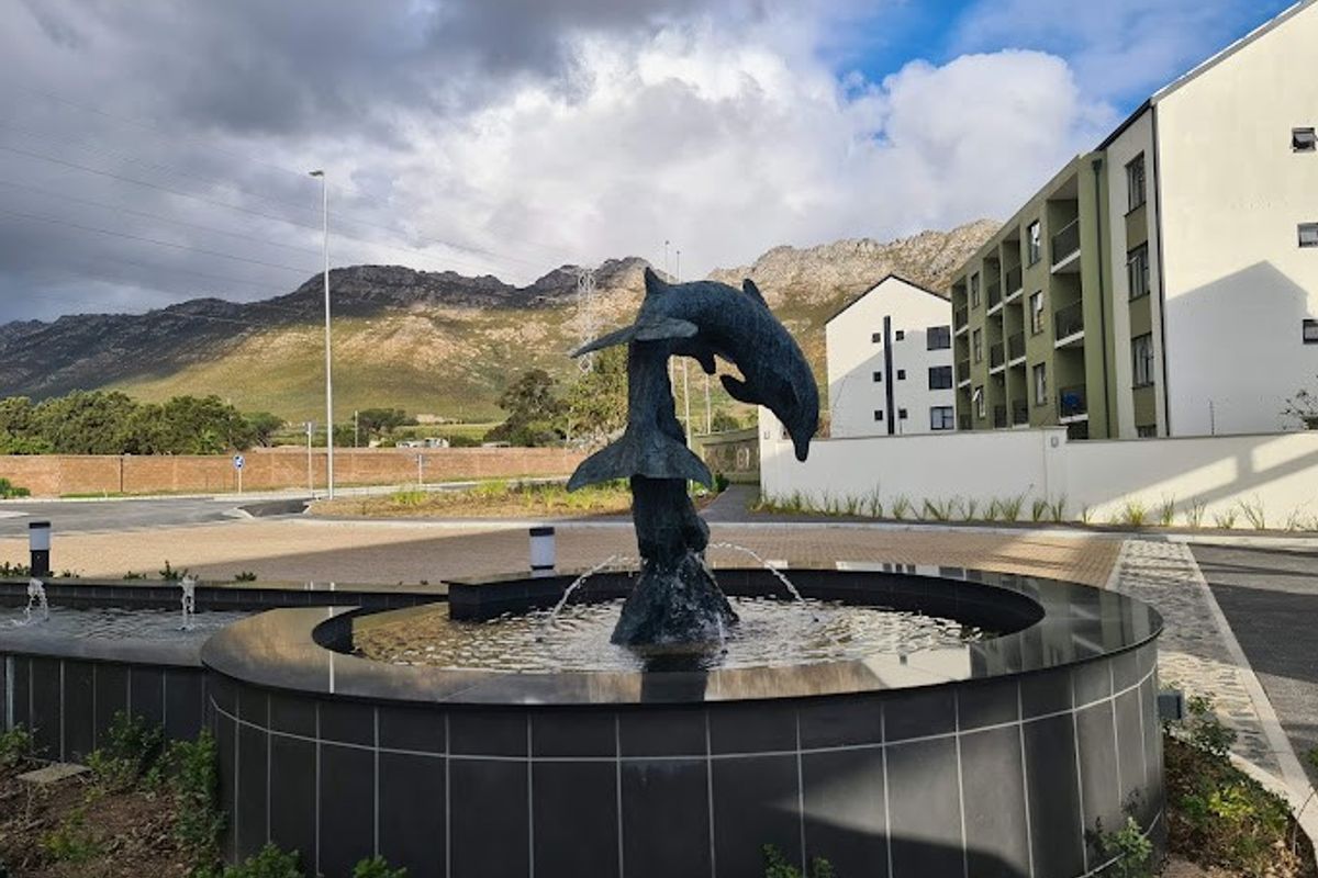 A well-maintained apartment complex entrance featuring a decorative dolphin water fountain, paved driveway, and scenic mountain views.