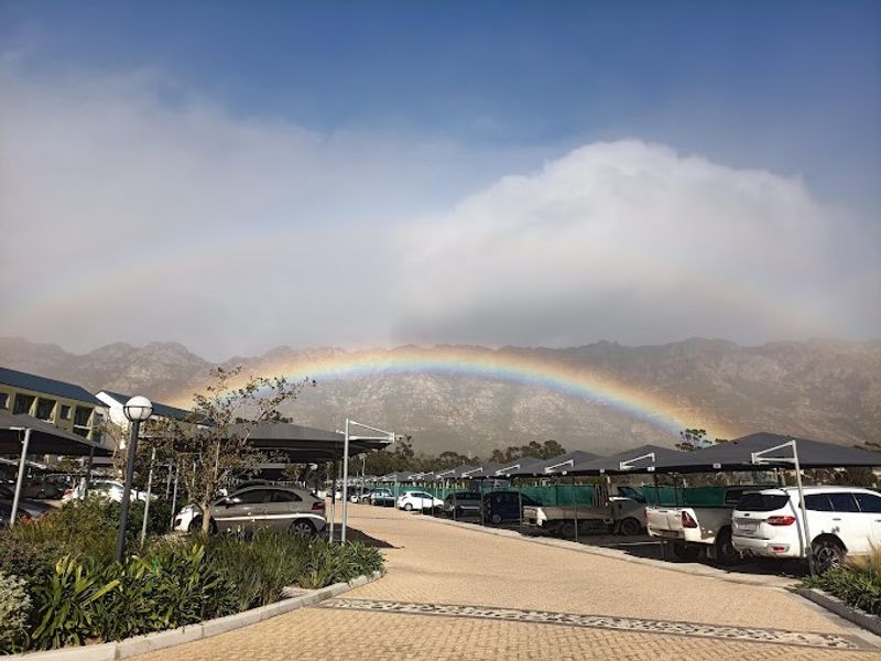 A well-maintained outdoor parking area featuring covered bays, paved driveways, and landscaped garden beds set against a scenic mountain backdrop.
