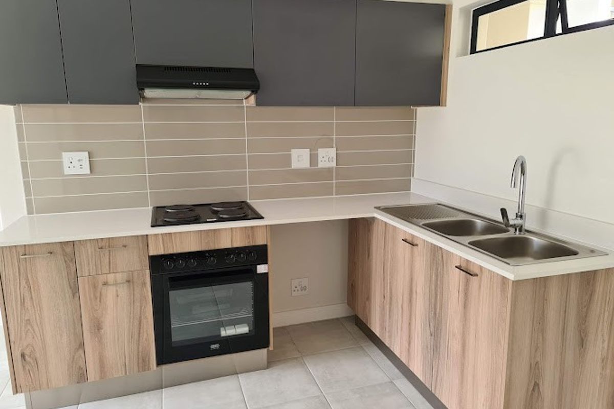 Modern kitchen featuring wood-grain lower cabinetry, dark grey upper cabinets, stone countertops, built-in oven, electric hob, and a double sink with tiled backsplash.