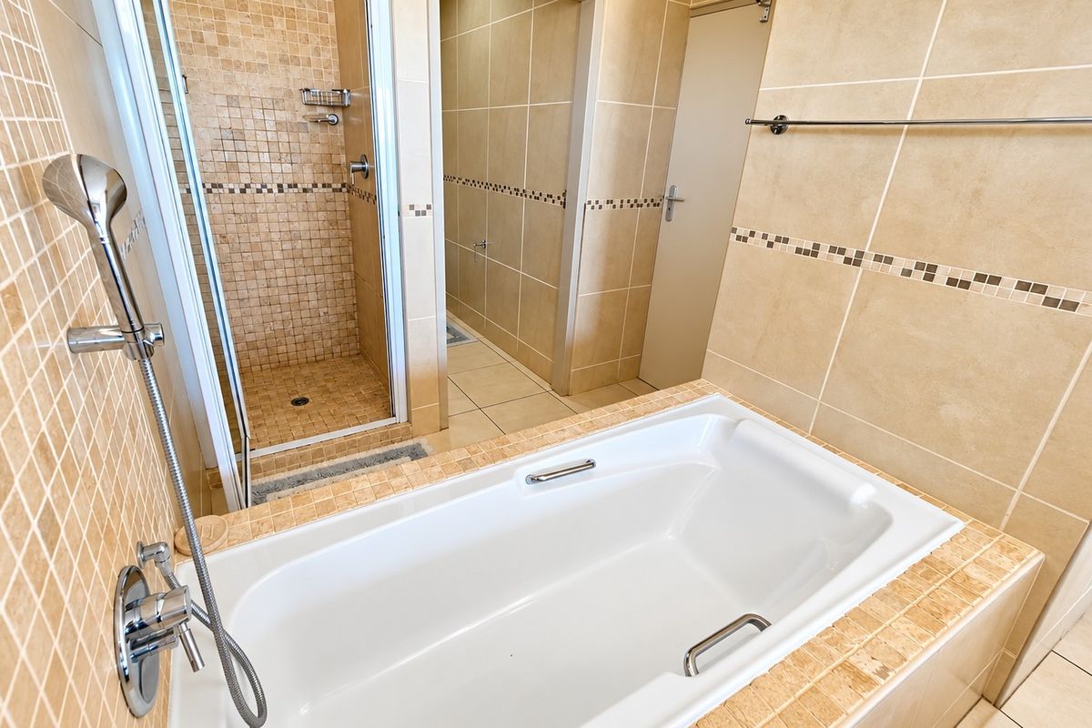 A clean, neutral-toned bathroom featuring a built-in bathtub, a separate shower enclosure with mosaic tiling, and ceramic floor tiles.