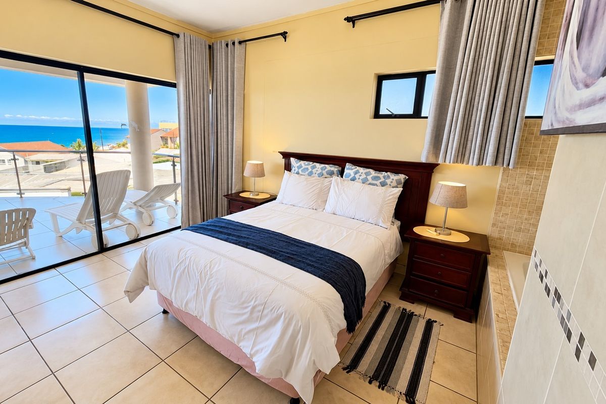 Spacious bedroom featuring tiled floors, an integrated bathtub, and large sliding glass doors opening onto a balcony with ocean views.