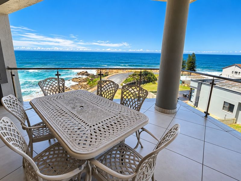 Spacious covered balcony featuring a built-in braai, modern glass balustrade, and expansive ocean views, perfect for outdoor entertaining.